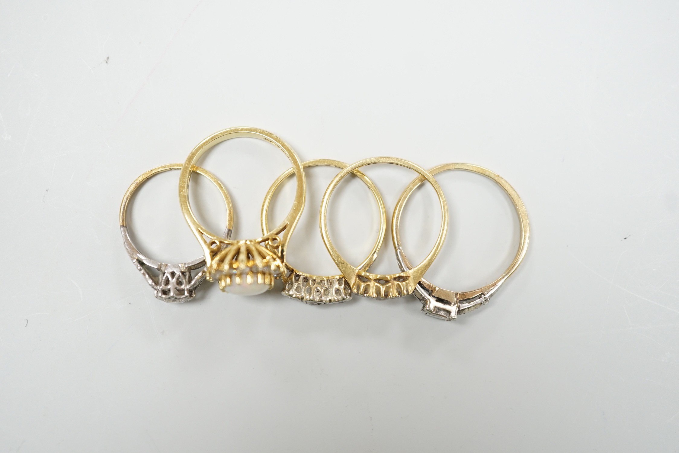 Four assorted 18ct and gem set dress rings, including white opal and diamond and two three stone diamond and one yellow metal and single stone diamond set ring, gross weight 14.3 grams.